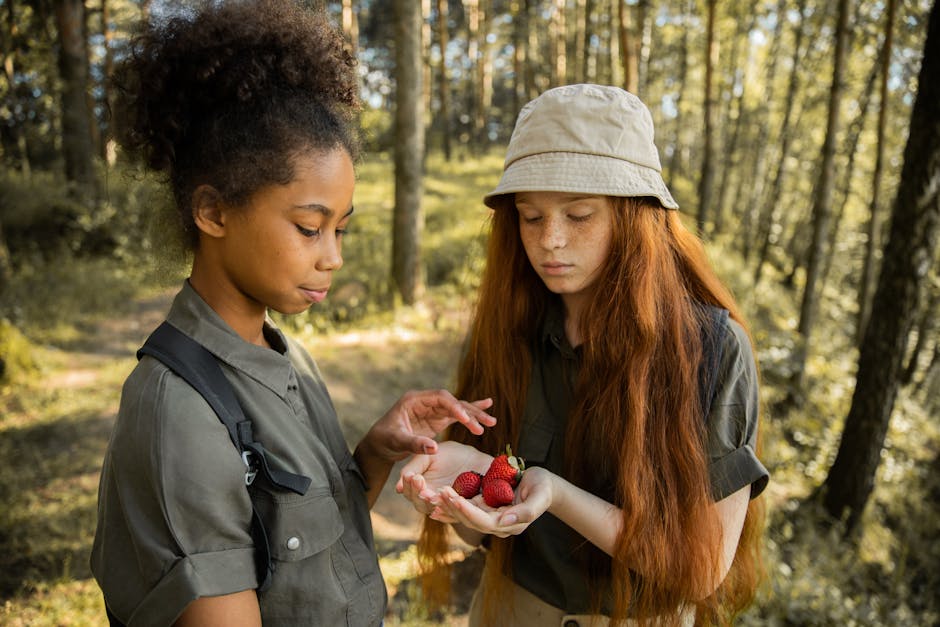 Two girls in the forest holding strawberries, enjoying a summer adventure